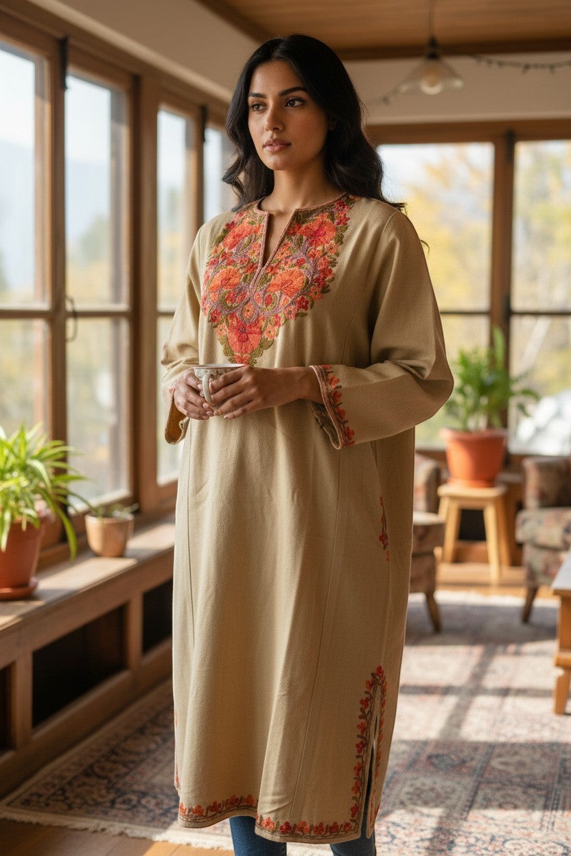 Kashmir Gallery beige woolen pheran with intricate traditional Aari embroidery on neckline and cuffs. Model holding a mug.